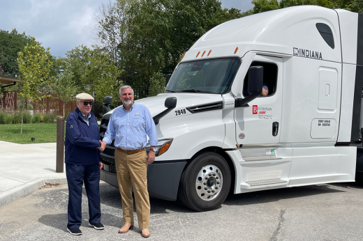 Owner Geary Buchanan and Indiana Governor Eric Holcomb shake hands in front of a Buchanan truck with the "IN Indiana" campaign words on the side.