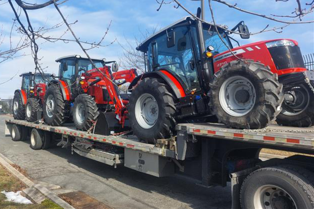 Multiple tractors and farm machinery being loaded on a stepdeck trailer to be transported to a retailer by Buchanan Logistics.