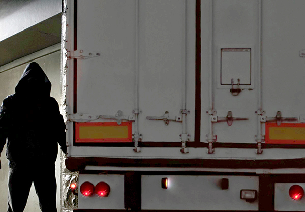 A thief prowls around a semi truck trailer to steal freight.